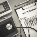 Top view health insurance form eyeglasses and pulse gauge with stethoscope on wooden background.