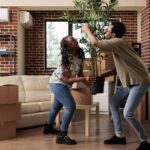 African american couple decorating new apartment to move in, unpacking plant and furniture in living room. Relocating household property after buying first house together, life event.